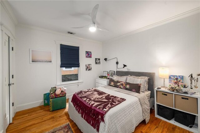 bedroom featuring a ceiling fan, baseboards, wood finished floors, visible vents, and ornamental molding