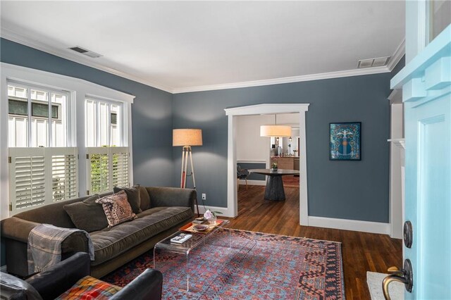 living area with baseboards, visible vents, ornamental molding, and wood finished floors