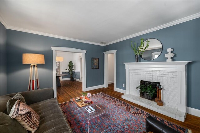 living room with visible vents, crown molding, a brick fireplace, wood finished floors, and baseboards