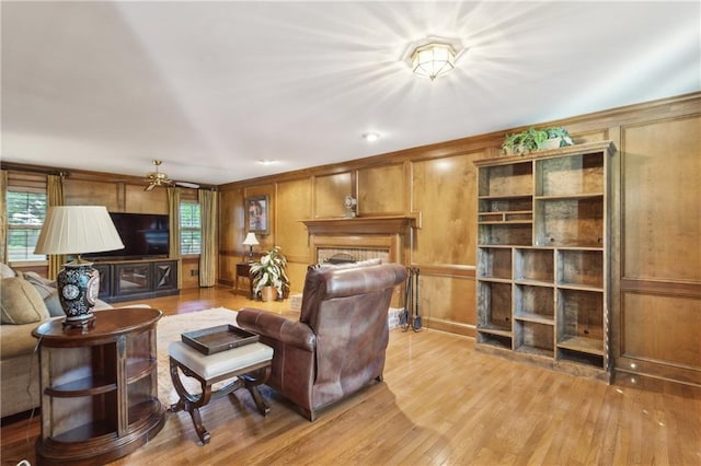 living room with healthy amount of natural light, light wood-style flooring, a fireplace, and wooden walls