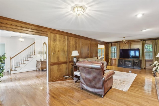 living area with light wood-style floors, stairs, wood walls, and ornamental molding