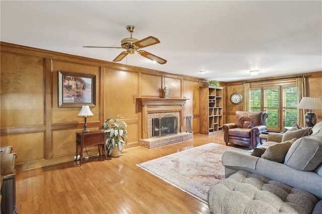 living room with a ceiling fan, light wood-type flooring, a brick fireplace, and a decorative wall