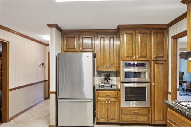 kitchen featuring stainless steel appliances, ornamental molding, brown cabinets, tasteful backsplash, and dark stone counters