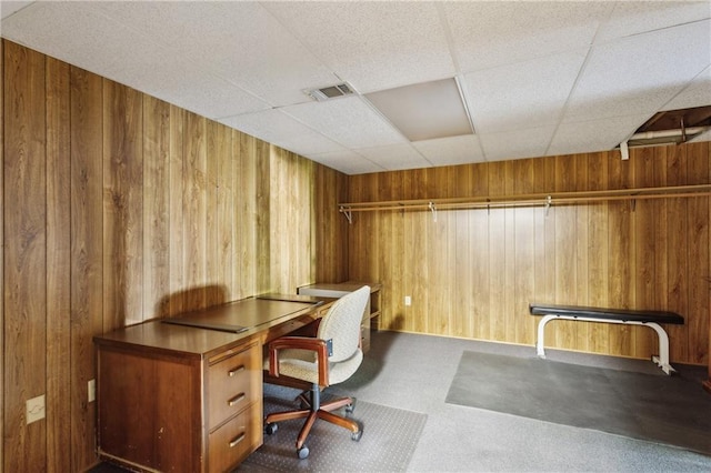 carpeted home office featuring wooden walls and a paneled ceiling