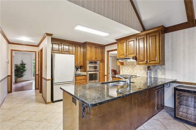 kitchen featuring freestanding refrigerator, a sink, double oven, under cabinet range hood, and a peninsula