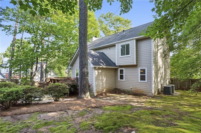 rear view of house featuring fence, cooling unit, and a shingled roof