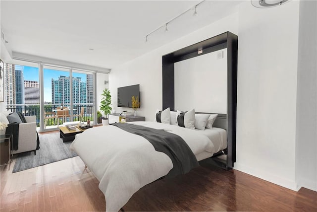 bedroom with access to outside, hardwood / wood-style floors, and rail lighting