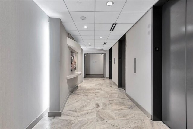 corridor with a drop ceiling, elevator, and light tile patterned floors