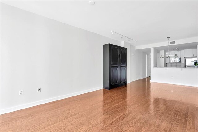 unfurnished living room with rail lighting, a notable chandelier, and wood-type flooring