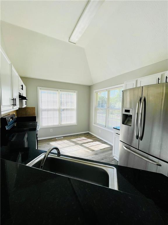 350 Fall View Ct, Winder, GA 30680 - kitchen with stainless steel fridge with ice dispenser, lofted ceiling, stove, white cabinets, and under cabinet range hood