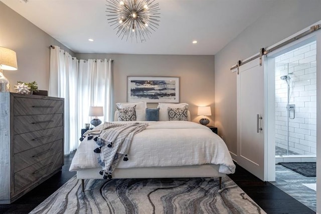 bedroom featuring connected bathroom, a barn door, dark hardwood / wood-style floors, and an inviting chandelier