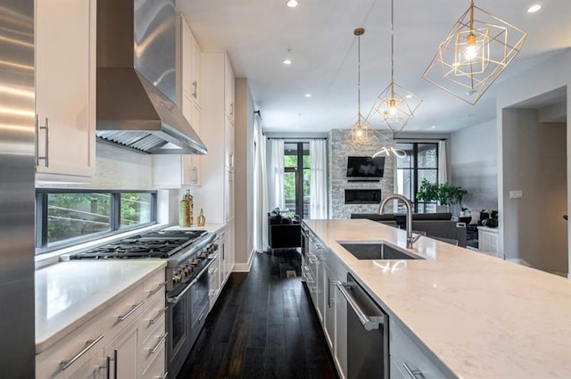 kitchen with sink, wall chimney exhaust hood, appliances with stainless steel finishes, decorative light fixtures, and white cabinetry