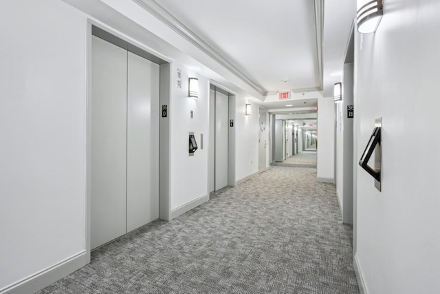 hallway with elevator, baseboards, and carpet flooring