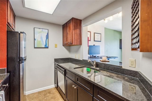 kitchen featuring light tile patterned floors, dark stone counters, a sink, freestanding refrigerator, and dishwasher