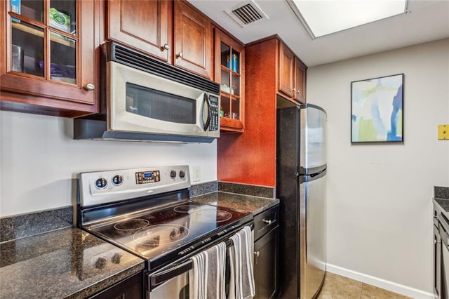 kitchen featuring light tile patterned floors, visible vents, baseboards, glass insert cabinets, and appliances with stainless steel finishes