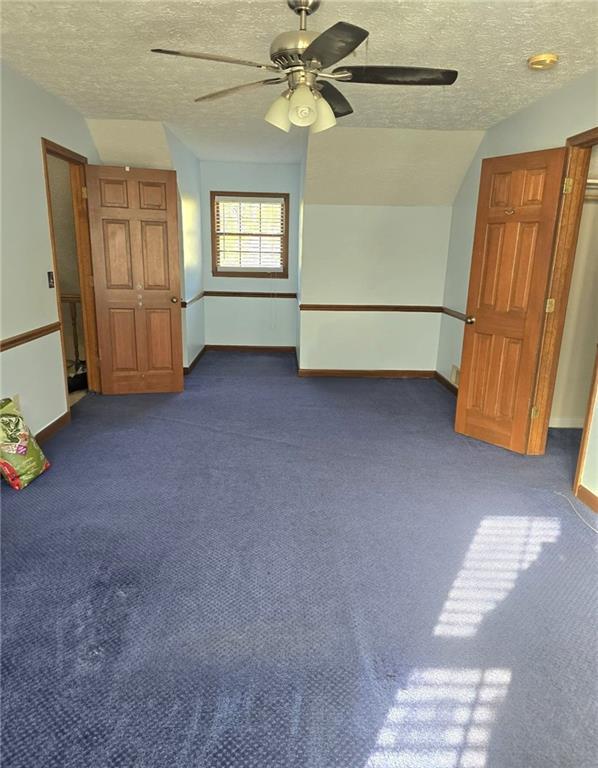 unfurnished bedroom with a textured ceiling, dark carpet, ceiling fan, and lofted ceiling