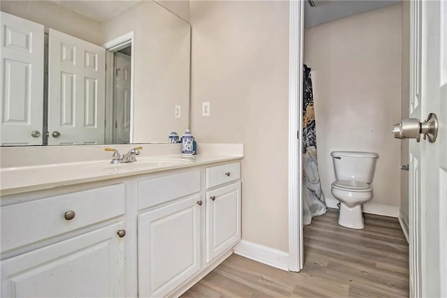 bathroom with vanity, toilet, wood finished floors, and baseboards