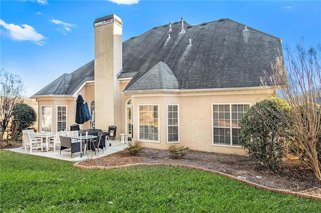 back of property with stucco siding, a lawn, roof with shingles, a chimney, and a patio area