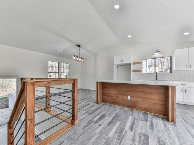 kitchen with lofted ceiling, white cabinetry, backsplash, and decorative light fixtures