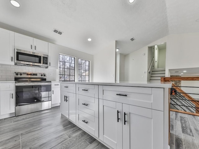 kitchen with white cabinetry, stainless steel appliances, backsplash, a textured ceiling, and lofted ceiling