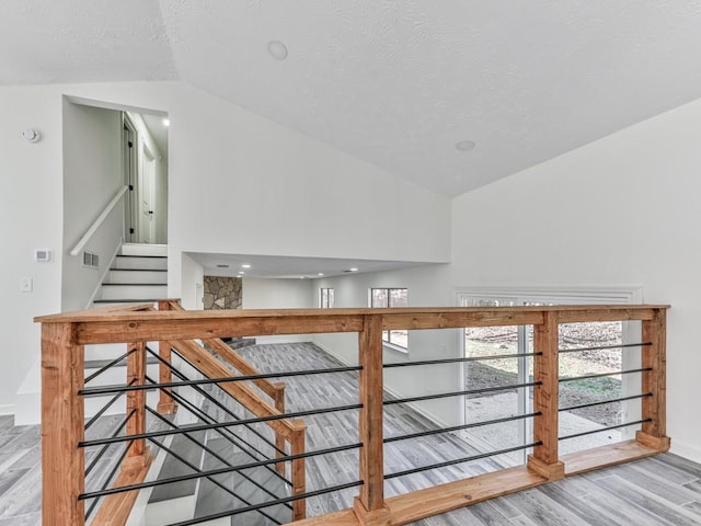 stairs with wood-type flooring, a textured ceiling, and vaulted ceiling