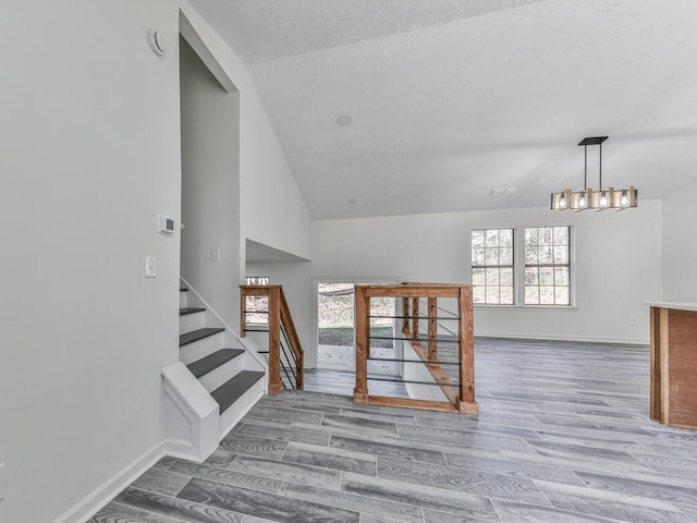 stairway with a textured ceiling, hardwood / wood-style flooring, lofted ceiling, and a notable chandelier