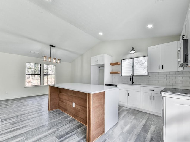 kitchen with pendant lighting, lofted ceiling, white cabinets, sink, and a kitchen island