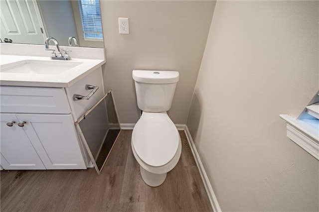 half bathroom with baseboards, vanity, toilet, and wood finished floors