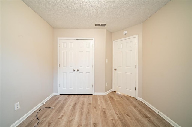 unfurnished bedroom with a textured ceiling, light wood-style flooring, visible vents, baseboards, and a closet