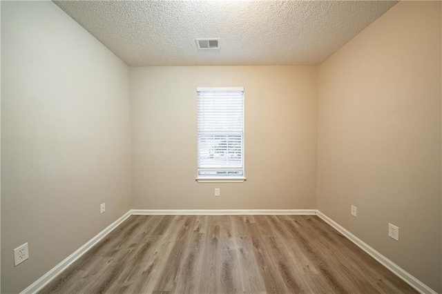 spare room featuring light wood-type flooring, visible vents, a textured ceiling, and baseboards