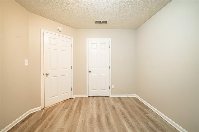 empty room featuring light wood-type flooring, visible vents, a textured ceiling, and baseboards