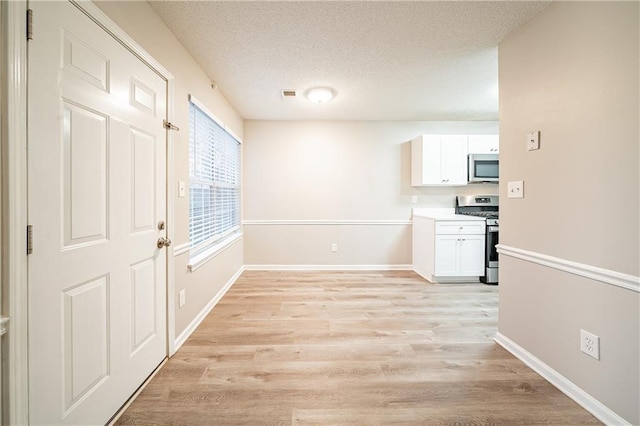 interior space with a textured ceiling, light wood finished floors, visible vents, and baseboards