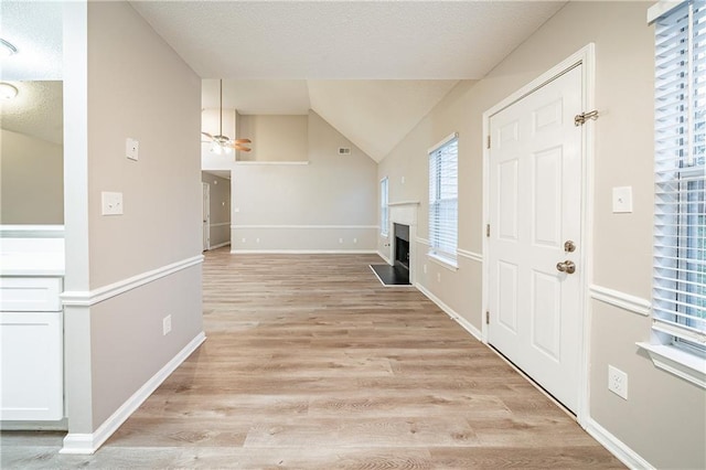 foyer featuring baseboards, lofted ceiling, ceiling fan, light wood-type flooring, and a fireplace