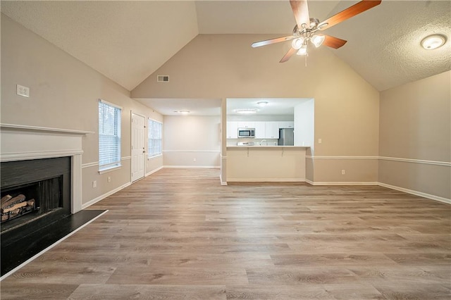 unfurnished living room with a fireplace with raised hearth, a ceiling fan, visible vents, baseboards, and light wood-type flooring