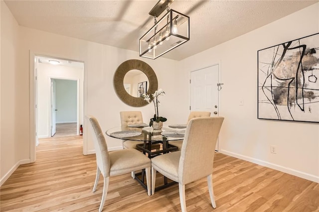 dining space with light wood-type flooring, baseboards, and a textured ceiling