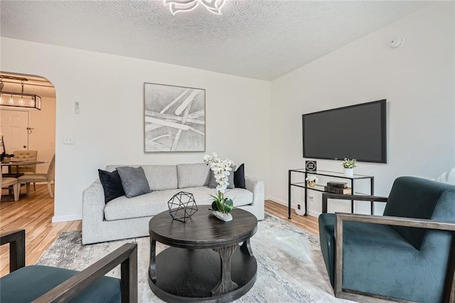 living area with wood finished floors, arched walkways, a textured ceiling, and baseboards