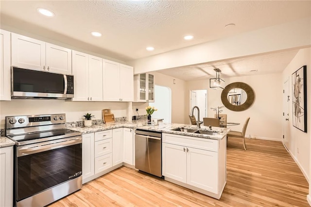 kitchen with stainless steel appliances, a peninsula, a sink, white cabinetry, and light wood-style flooring