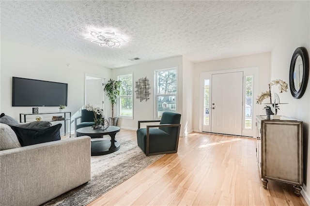 living area featuring light wood-style flooring, a textured ceiling, and baseboards