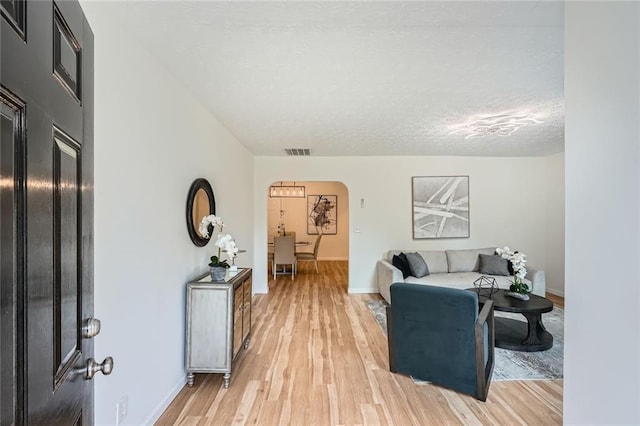 living area with arched walkways, light wood-type flooring, baseboards, and a textured ceiling