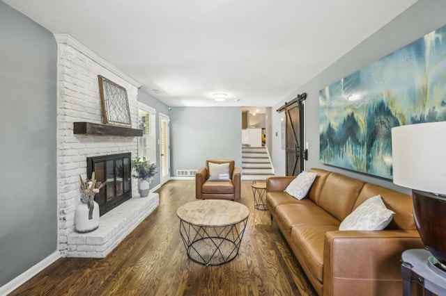 living area featuring a barn door, a brick fireplace, wood finished floors, and baseboards