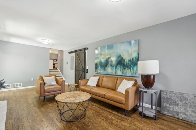 living area with wood finished floors, visible vents, baseboards, and a barn door