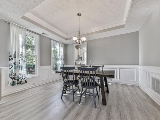 dining area with a tray ceiling, a chandelier, a textured ceiling, and light wood-type flooring