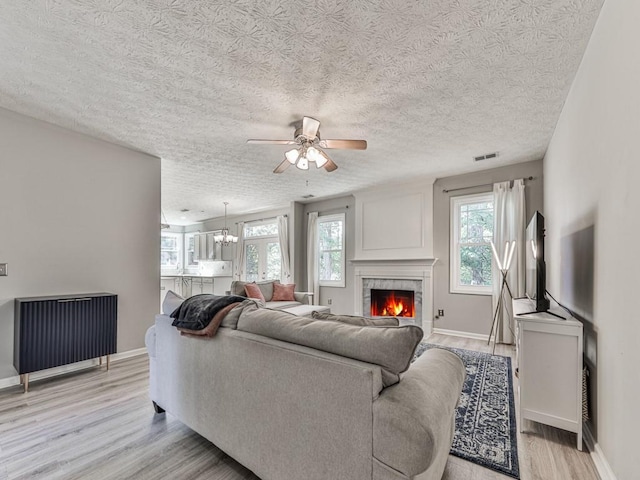 living room with a tile fireplace, a textured ceiling, ceiling fan with notable chandelier, and a wealth of natural light