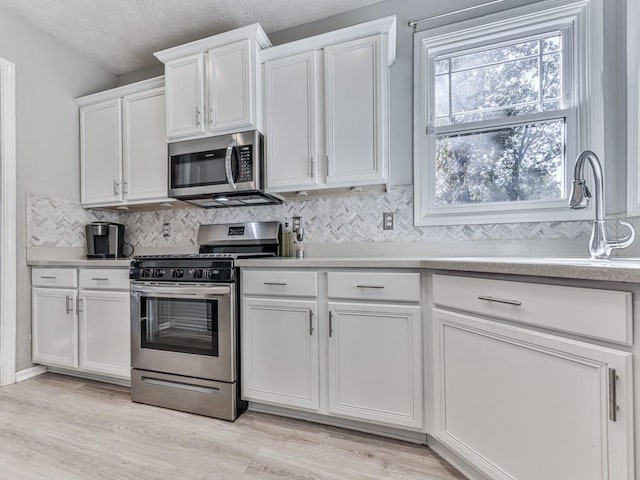 kitchen with backsplash, white cabinets, sink, light hardwood / wood-style flooring, and appliances with stainless steel finishes