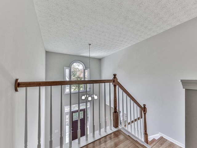 stairs featuring wood-type flooring, a textured ceiling, and an inviting chandelier