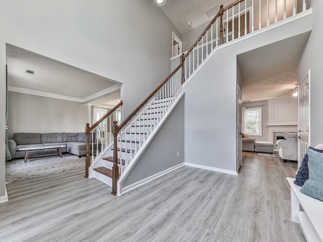 stairs featuring a towering ceiling, ornamental molding, and hardwood / wood-style flooring