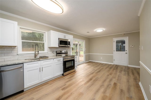 kitchen with appliances with stainless steel finishes, a sink, decorative backsplash, light wood-style floors, and white cabinets