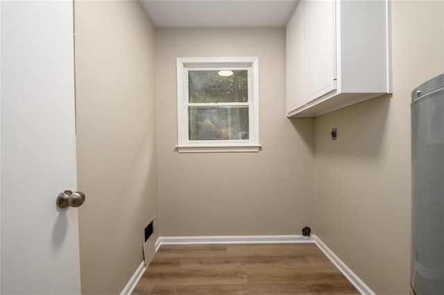 laundry room featuring cabinet space, wood finished floors, baseboards, and water heater