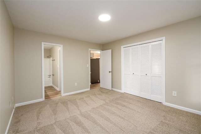 unfurnished bedroom featuring light colored carpet, a closet, baseboards, and ensuite bath