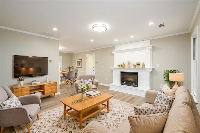 living area with light wood finished floors, ornamental molding, recessed lighting, and a glass covered fireplace